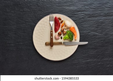 20: 4 concepto de dieta de ayuno. Un tercer plato con comida sana y dos tercios platos están vacíos. Ternera, salmón, huevo, brócoli, tomate, nueces, zanahorias, champiñones. Fondo oscuro. Vista superior.