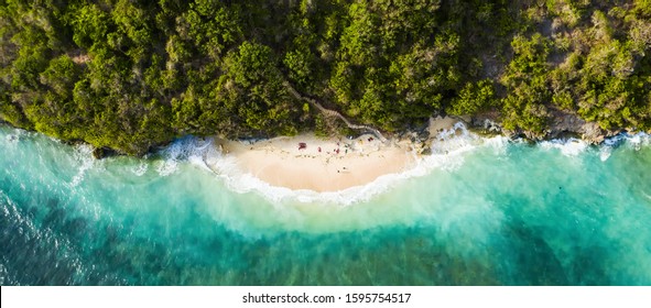 上からの眺め、日没時にターコイズブルーの荒れた海に浸かる美しいビーチ、グリーンボウルビーチ、南バリ、インドネシアで日光浴をしている何人かの観光客の見事な空中写真。