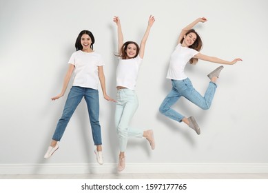 Nhóm phụ nữ trẻ mặc quần jeans thời trang nhảy gần bức tường sáng