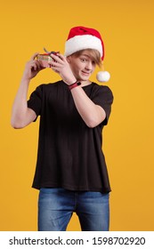 Chico joven con un sombrero rojo de santa tiene una caja de regalo en sus manos y posa sobre un fondo amarillo