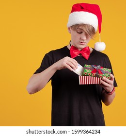 Un joven con un sombrero rojo de Papá Noel sostiene en sus manos billetes, dinero y posa sobre un fondo amarillo