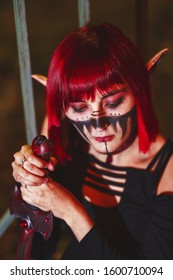 Girl cosplay in the image of a dark elf in a red wig portrait close-up. A woman with red lenses in her eyes and red hair in an elf costume with false ears and makeup. Dark elf outfit for Halloween.