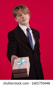 Un joven adolescente con una chaqueta negra sostiene una caja con un regalo en un fondo rojo