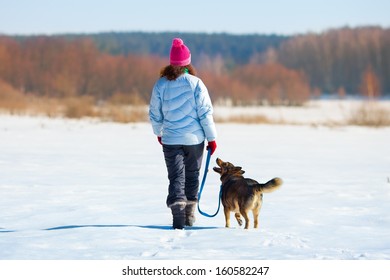 Young woman with her dog walking on the snowy field