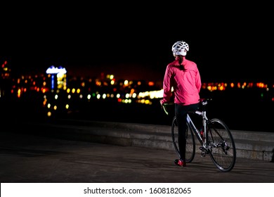 Young Woman Cyclist Resting with Road Bike and Looking at Night City Lights at Cold Autumn. Healthy Lifestyle and Urban Sport Concept.