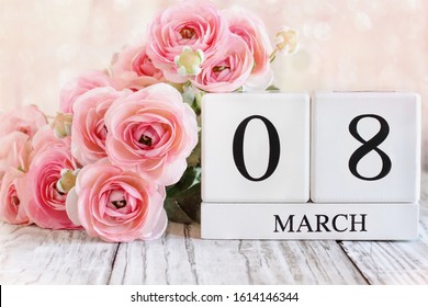 White wood calendar blocks with the date March 08 for International Women's Day and pink ranunculus flowers over a wooden table.