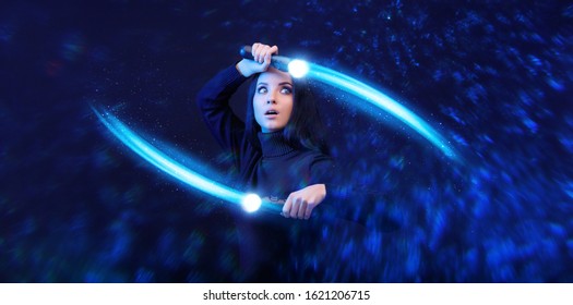 Beautiful young woman in futuristic dress over dark background. Gamer girl with controllers in hands. Augmented reality, game, hobby concept. VR. Blue neon light.