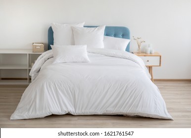 ソファに白いベッド リネンのインテリア。ベッド、白い寝具、ベッドサイド テーブルのある寝室。青いヘッドボード付きのベッドに白い枕、羽毛布団、羽毛布団ケース。正面図。
