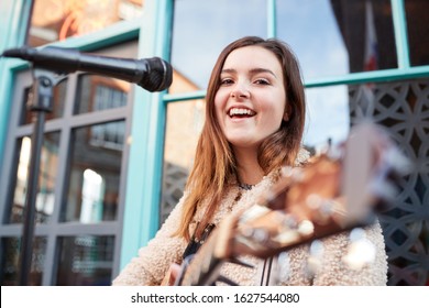 ภาพหญิงสาวนักดนตรีเล่นกีตาร์อะคูสติกและร้องเพลงอยู่ริมถนน