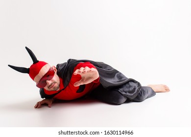 Potret konseptual pria iblis yang kalah dan tak berdaya dengan kostum vampir merah hitam meminta bantuan dan belas kasihan sambil berbaring di tanah di studio dan mengulurkan tangannya.
