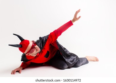 Potret konseptual pria iblis yang kalah dan tak berdaya dengan kostum vampir merah hitam meminta bantuan dan belas kasihan sambil berbaring di tanah di studio dan mengulurkan tangannya.