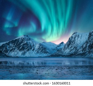Aurora borealis über den schneebedeckten Bergen, der Küste des Sees und dem Spiegelbild im Wasser. Nordlichter über schneebedeckten Felsen. Winterlandschaft mit Polarlichtern, Fjord. Sternenhimmel mit heller Aurora