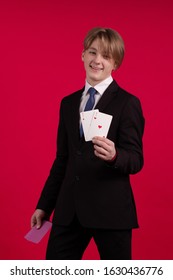 Teenager boy in a black jacket holds playing cards for poker and tricks in his hands and poses on a red background