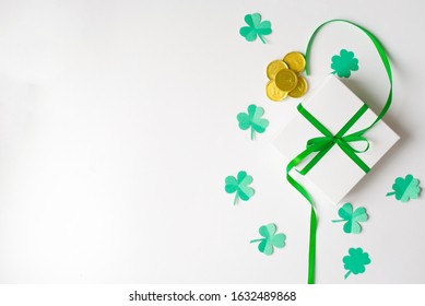 Komposisi untuk Hari St. Patrick. Kotak hadiah putih dengan pita satin hijau, semanggi dan koin emas mainan dengan latar belakang putih. Pemandangan dari atas, berbaring datar, menyalin ruang