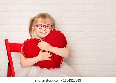 Una ragazza con sindrome di Down su uno sfondo bianco con un cuore fatto a mano. Nello studio. Muro di mattoni.