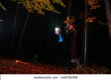 Zauberer (Zauberer), der im magischen Wald einen Zauber wirkt. Hält seinen magischen Stab. Magische Beleuchtung. Herbstferienfeier. Geheimnis und Albtraumkonzept