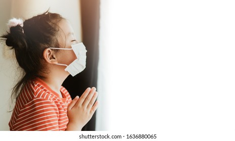 Weinig Chinees meisje dat masker draagt ter bescherming van pm2.5 en coronavirus Covid-19. Blijf thuis biddend tot God. Online kerkverering in zondag. Weinig Aziatisch meisje hand bidden thuis. Sociale afstand nemen.