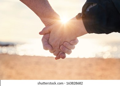 Close up of elderly couple holding hands on the beach at sunset