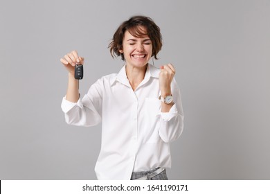 Lächelnde junge Geschäftsfrau im weißen Hemd posiert isoliert auf grauem Wandhintergrund Studioportrait. Leistungskarriere Reichtum Geschäftskonzept. Mock-up-Kopienbereich. Autoschlüssel mit Gewinnergeste halten