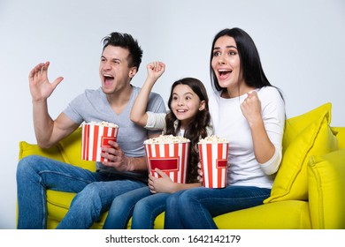 Enjoying adventures. Overjoyed family are watching movies at home, sitting on a big yellow sofa together and screaming, while eating popcorn.