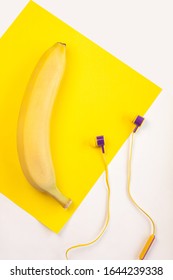 Fruta de plátano plana amarilla y auriculares en el espacio de copia de fondo blanco, vista superior. Telón de fondo de primavera verano, concepto de colores púrpura de moda, sol brillante. Banner de música, diseño de publicidad de medios cosial.