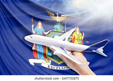 Airplane in hand with national flag State of New York on a background of blue sky with sunbeams