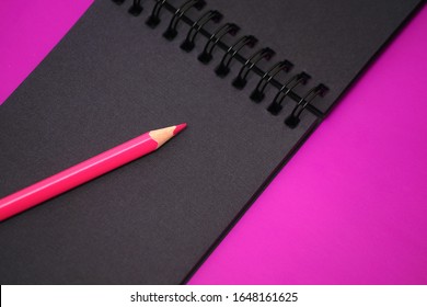 Black notebook with black sheets. Album and pencil on a purple background. Notebook sketch for the artist. Sketchbook with a spiral. Stylish bright background.
