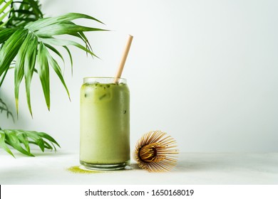 Membuat es matcha latte Jepang, teh hijau dengan susu, susu kedelai, alat matcha tradisional, dengan sedotan bambu dalam gelas dengan latar belakang putih.