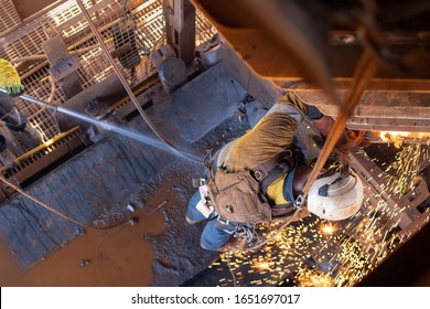Work safety practise spotter, firewatch personal holding firehose spraying water at the conveyor belt to controlling fire breakout during welder wearing PPE conducting oxy cutting metal repairing
