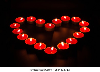 Rote brennende Kerzen in Form eines Herzens auf schwarzem Hintergrund.