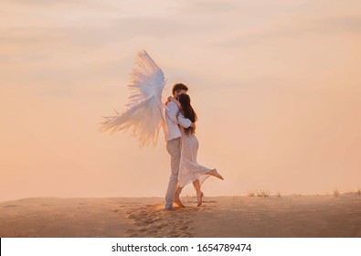 ポジティブハッピーガールと天使の抱擁。白いスーツを着た男 創造的な翼 王女の長い髪のピンクのドレス。バニラの空の雲、砂の日没の砂漠の足跡を背景に。ドバイ アラブ首長国連邦 自然