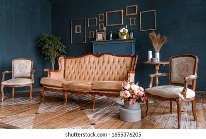 Modern dark interior with a fireplace, flowers, a cozy brown sofa with carved legs and two elegant armchairs. The stylization of the Baroque, classical design, historic interior.