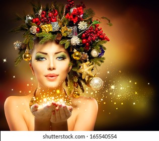 Zimowa kobieta w świątecznym nastroju z cudem w dłoni. Wróżka. Piękna fryzura i makijaż na Nowy Rok i choinkę. Magia. Piękna modelka dmuchająca magiczne gwiazdki.