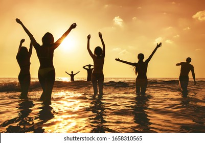 Eine große Gruppe glücklicher Völker steht am Sonnenuntergangsmeerstrand. Silhouetten mit erhobenen Armen