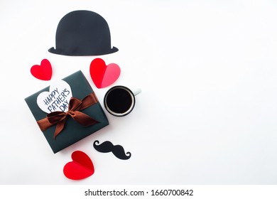 Konsep Cuti Hari Bapa. Topi Flatlay, cawan kopi, hadiah, hati merah dan misai hitam lucu pada latar belakang putih terpencil. Salin ruang untuk inskripsi.