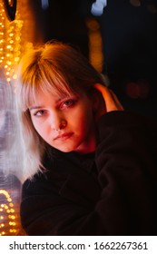 Closeup portrait of a beautiful blonde girl with long curly hair at night with neon lights of the evening city