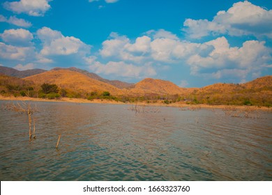 Dry trees and tree branches are dead in the middle of lake and beautiful mountain with dramatic clouds. Natural view of little dead trees in the reservoir. Beautiful view of dried trees in the lake.
