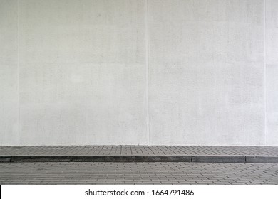 Großes modernes Gebäude mit hoher weißer Wand in der Nähe des leeren Bürgersteigs, der im Frühjahr mit grauen Steinfliesen auf der Stadtstraße bedeckt ist