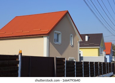 large private house with white windows under a red tiled roof behind a brown wooden fence against a blue sky on a sunny day