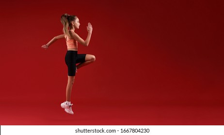 A cute kid, girl is engaged in sport, she is looking away while jumping. Isolated on red background. Fitness, training, active lifestyle concept. Horizontal shot. Side view. Web Banner