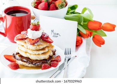 Nahaufnahme eines Stapels Pfannkuchen mit einer Karte, Blumen und Kaffee zum Muttertag. Ein Konzept zum Muttertag.