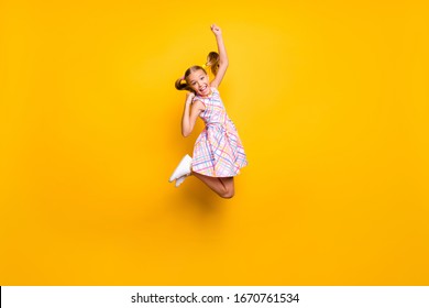 陽気な子供のジャンプの完全な長さの写真は、喜ぶ勝利の宝くじの売り上げを上げる拳を叫びますええ、市松模様のスカートの分離された明るい輝きの色の背景を着用してください