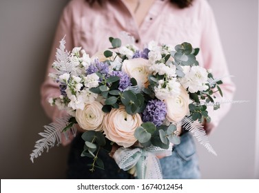 Sehr nette junge Frau, die einen großen und schönen Blumenstrauß aus frischen Ranunkeln, Matthiola, Nelken, Eukalyptus, japanischen trockenen Farnblumen in weißen und pastellvioletten Farben hält, Blumenstrauß aus nächster Nähe