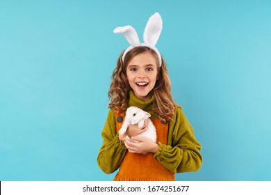 Cô bé mỉm cười mặc một chiếc váy đứng bị cô lập trên nền xanh, mừng lễ Phục sinh, ôm một chú thỏ