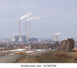 künstliche Landschaft der Autobahn, die in die Stadt führt, und ein Wärmekraftwerk mit rauchenden Schornsteinen am Horizont im zeitigen Frühjahr