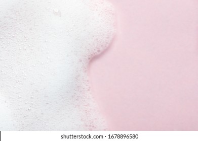 Schäumende Flüssigkeit auf rosafarbenem Hintergrund. Kosmetikschaumhintergrund mit Kopienraum auf der rechten Seite. Kosmetische Produktprobe von Mousse, Shampoo oder Seife. Hautpflege, Kosmetik und Schönheitskonzept