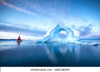 Velero con velas rojas navegando entre enormes icebergs durante el anochecer. Disko Bay, Groenlandia.
