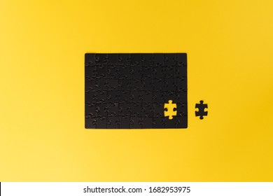 An unfinished black puzzle on a yellow background. The puzzle without one piece. Almost complete. Unfinished work concept