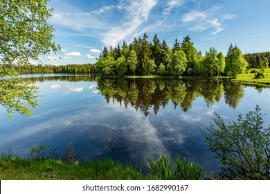 Schilderachtig uitzicht op een Kladska-meer in Tsjechië, dicht bij Marianske Lazne omgeven door bos. Zonnig zomerlandschap met blauwe lucht en witte wolken en reflectie in water.
