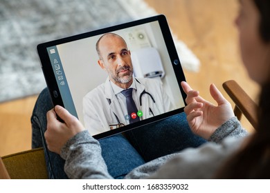 Bagfra af kvinde, der foretager videoopkald med sin læge, mens hun bliver hjemme. Nærbillede af patient i videokonference med praktiserende læge på digital tablet. Syg pige i online konsultation.